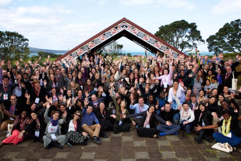 A large group of adults poses in front of an archway decorated with colorful designs