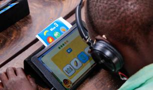 An African student with headphones on works on a tablet