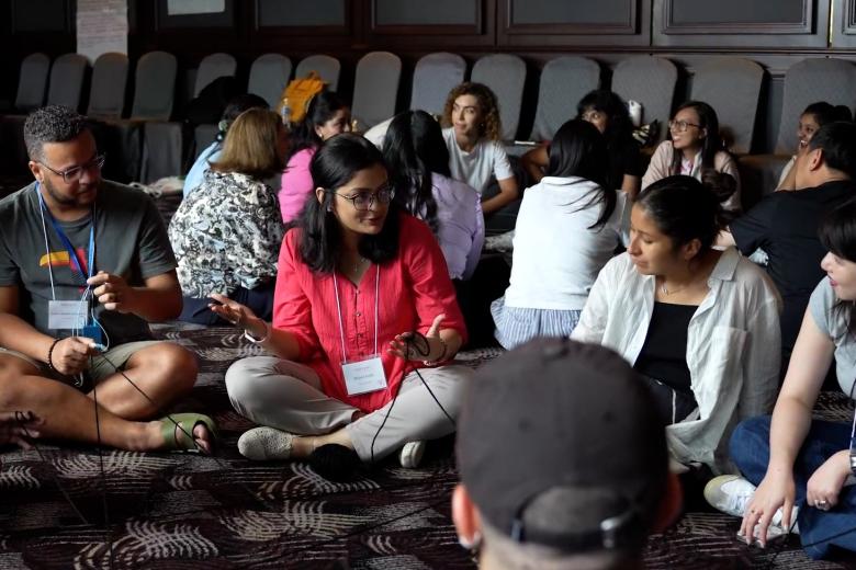 A diverse group of young adults sit cross legged in a semi-circle