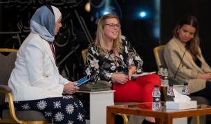 Three women sit on stage for a panel with microphones in front of them