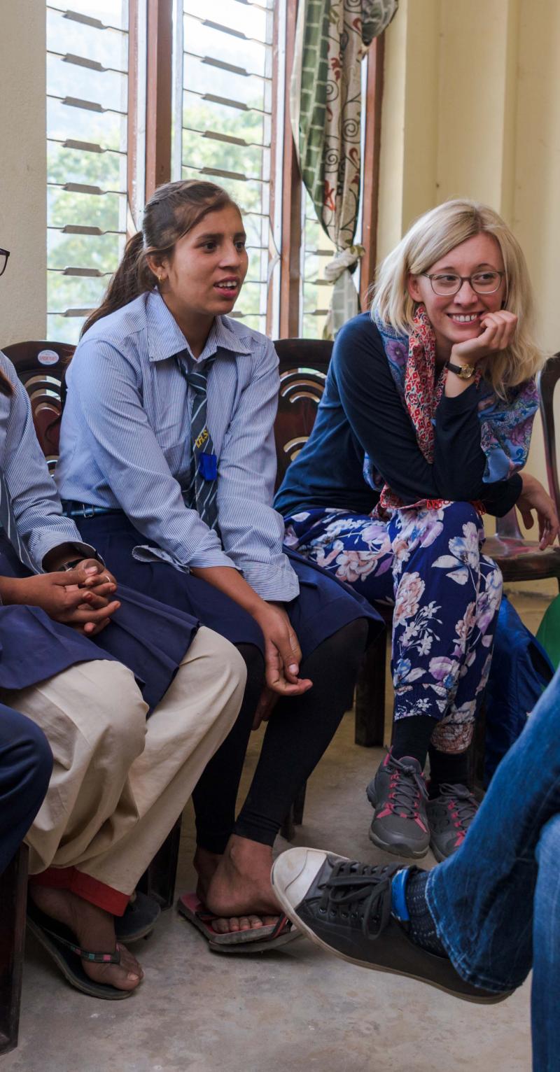 A group of four Asian girls and three European women are seated in a half-circle talking to each other