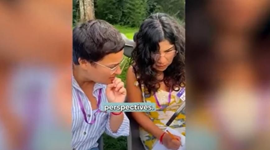 Two women with brown hair look at a paper together