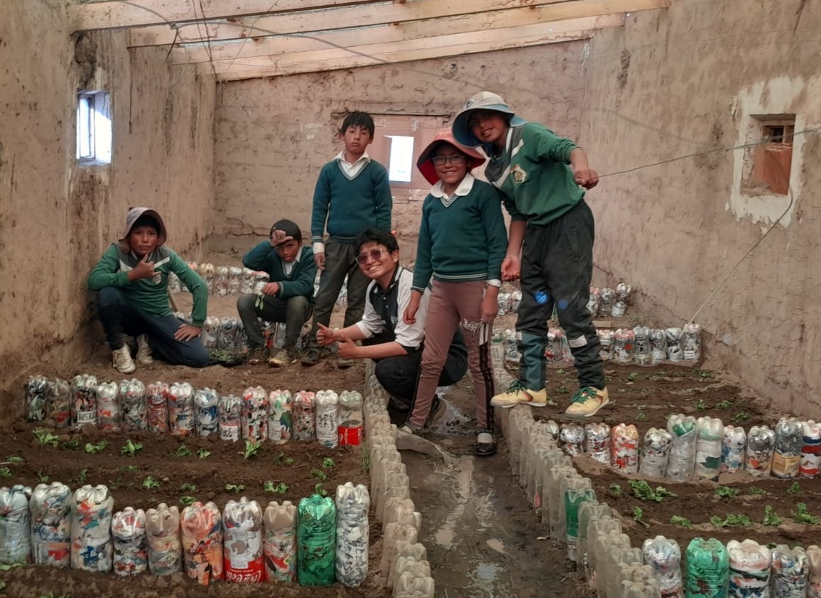 Five boys and one young man with brown hair and tan skin pose in a garden in which plastic bottles are used as decoration