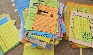 A hand-written letter on orange paper with the word Palestine at the top and a drawing of a Palestinian flag sits atop a pile similar letters on colorful paper