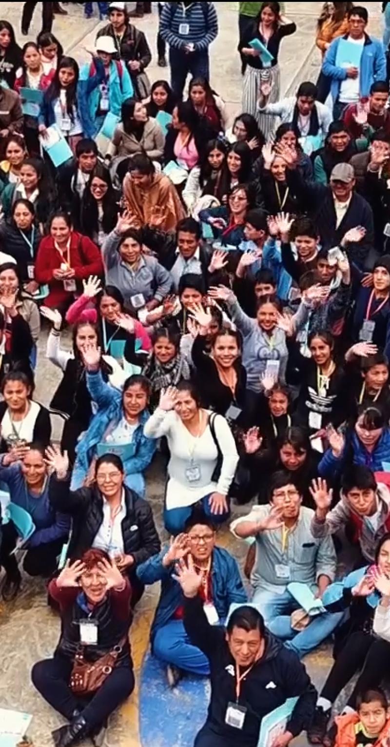 Shot from above, a large crowd of people in an outdoor courtyard look up at the camera