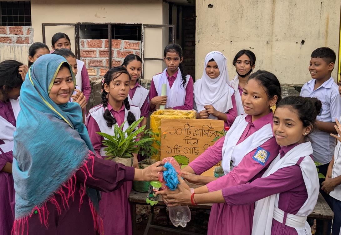 A group of South Asian girls in purple school uniforms with white sashes surrounds a project