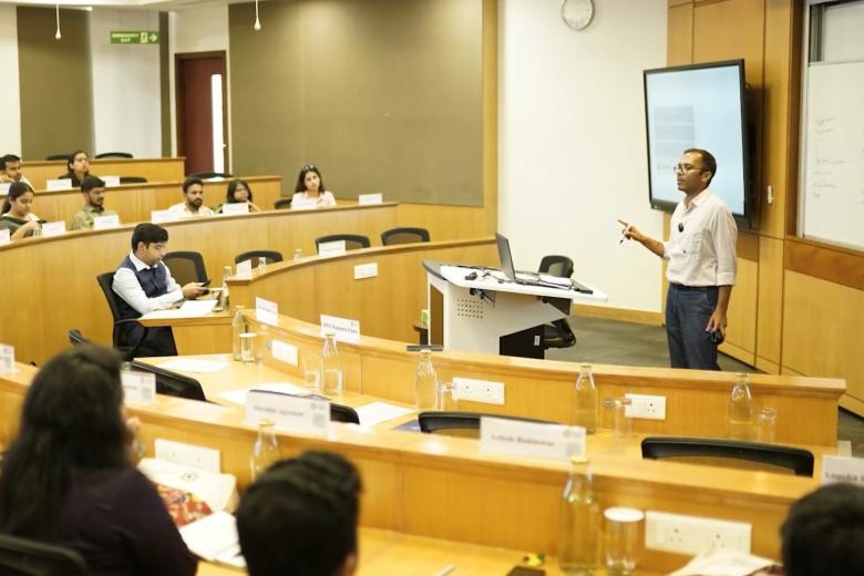 An Indian man speaks in front of rows of seats that appear to be in a government body