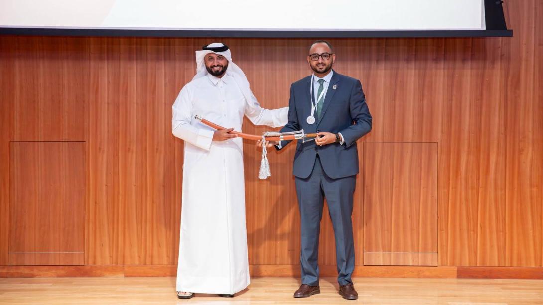Two men in formal dress onstage holding an award