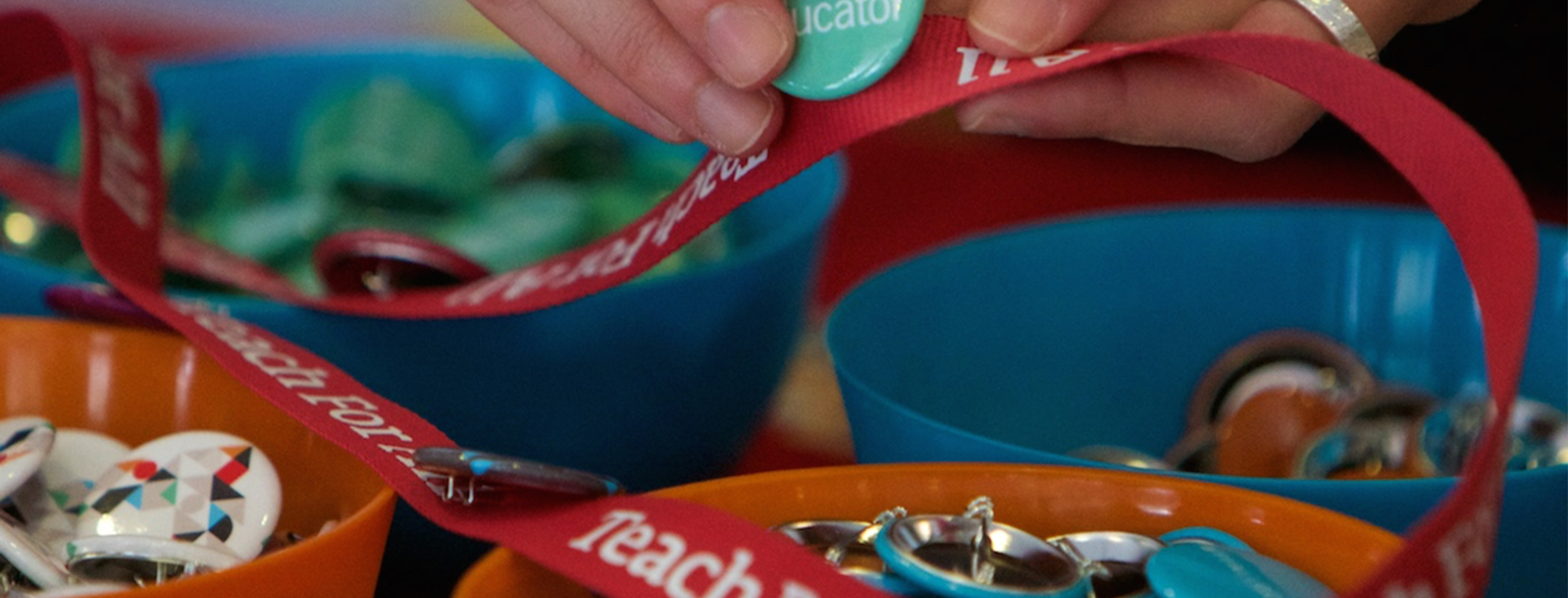 Close-up of a hand pinning a green button to a red Teach For All lanyard